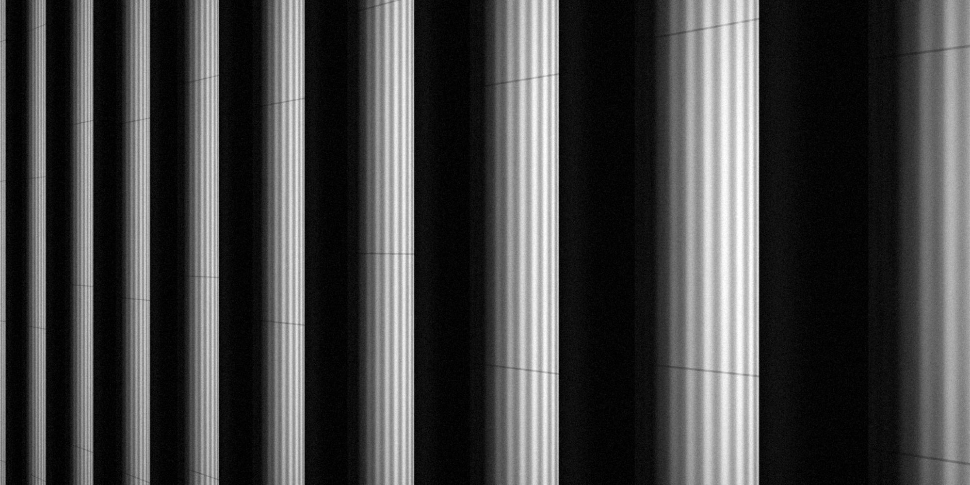 Fluted stone columns in strong side light, in black and white.