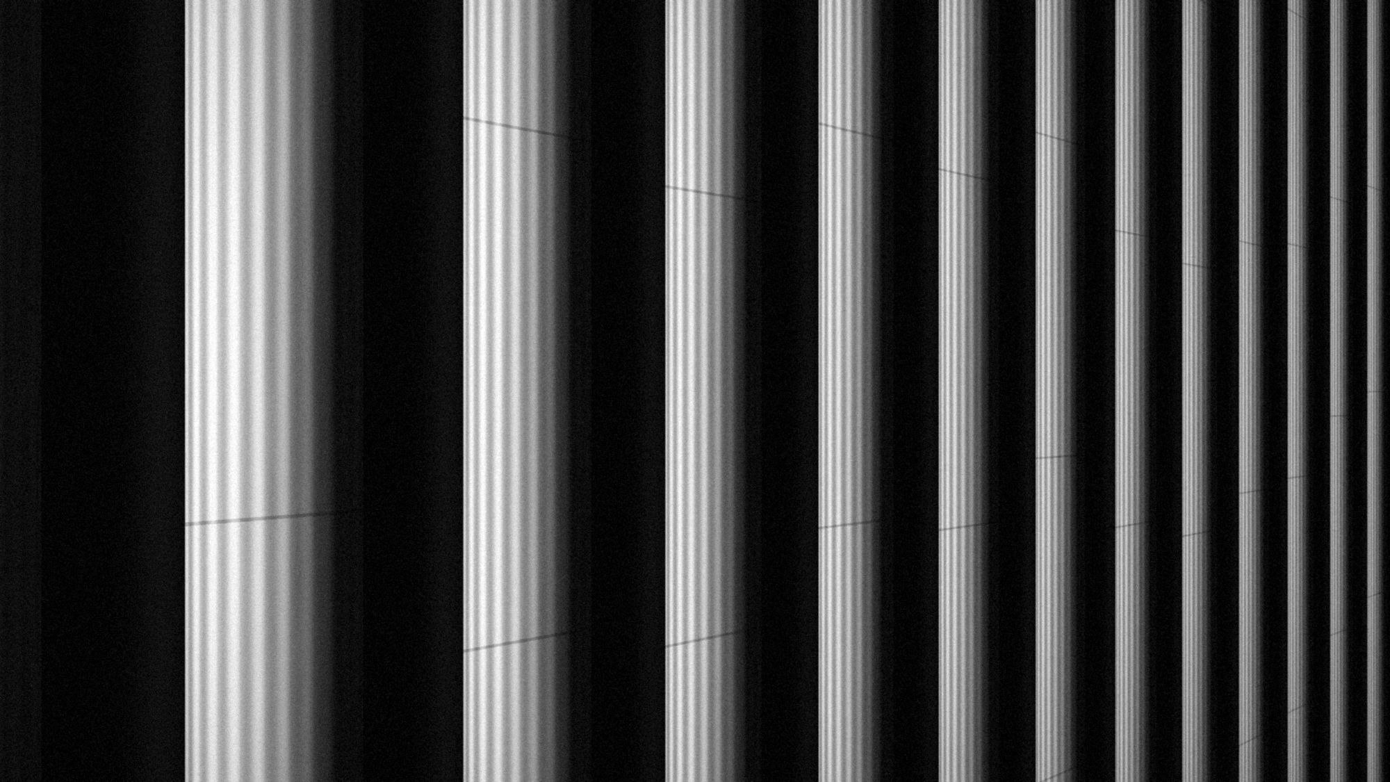 A row of fluted stone columns receding into shadow, in black and white.