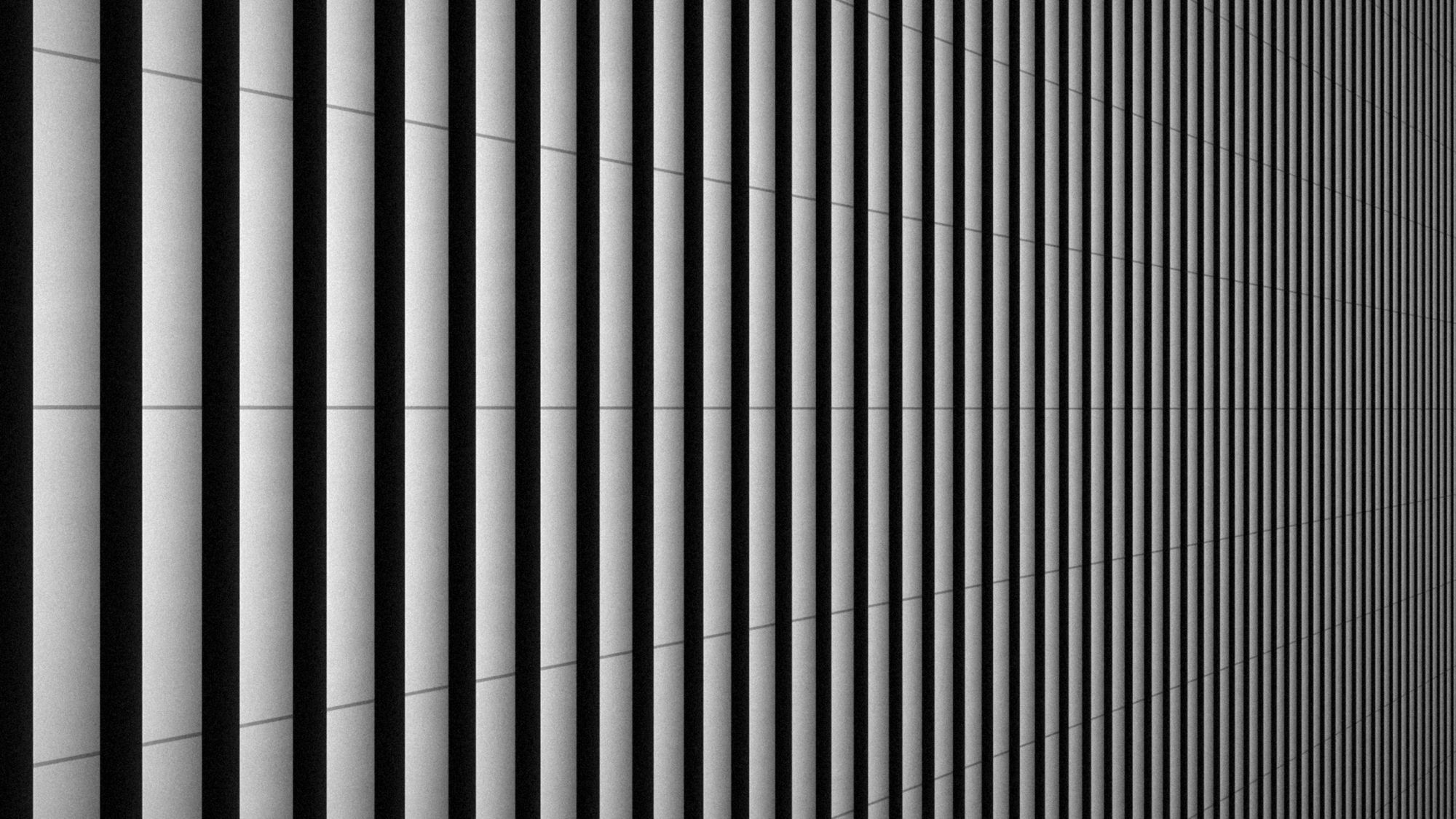 A facade of deep vertical fins receding into shadow, in black and white.