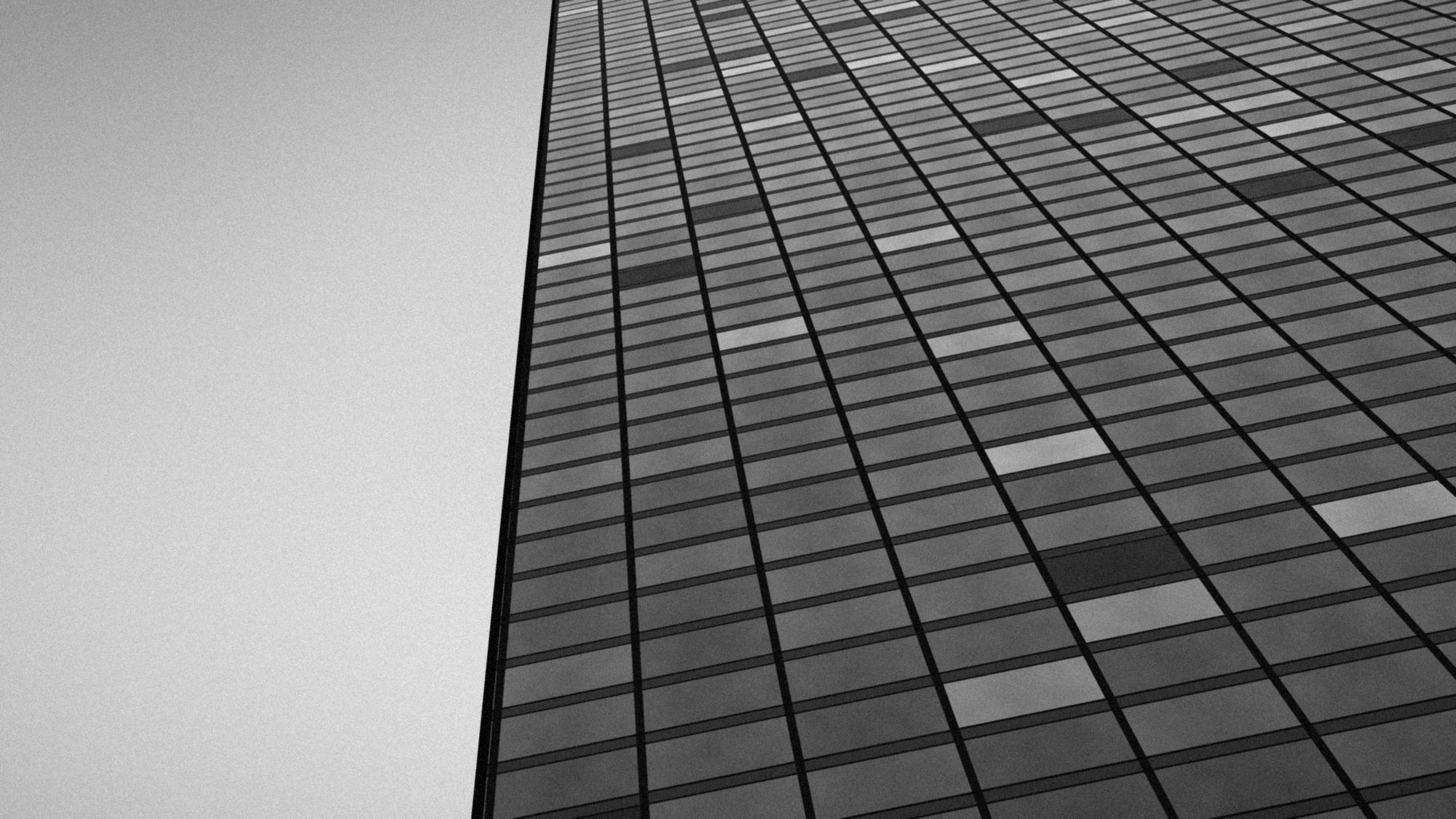 Looking up the glass curtain wall of an office tower, in black and white.