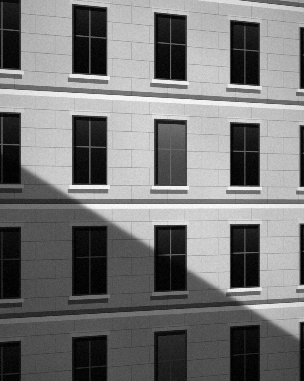 A stone civic facade with tall windows, crossed by a long diagonal shadow.